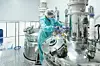 Pharmaceutical factory woman worker in protective clothing operating production line in sterile environment