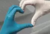 Zwei Hände in Latexhandschuhen, links blau und rechts weiß, formen mit den Fingern ein Herz.