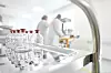 Labor mit Glasflaschen im Vordergrund und Personen in Schutzkleidung im Hintergrund