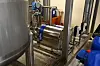 Edelstahlbehälter mit blauem Band in einer Industrieanlage zwischen Rohren und Metallrahmen.