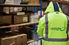 Person in gelber Warnschutzjacke vor Lagerregalen mit Kartons und Movianto-Logo.