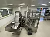 Industrielle Abfüllmaschine in einem hellen Produktionsraum mit Edelstahlflächen und Rollwagen.