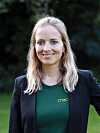 Porträt von Dr. Anne Lamp im Freien vor dunklem, unscharfem Hintergrund mit grünem Shirt und schwarzem Blazer.