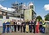 Gruppe von Menschen mit Schutzhelmen steht vor einer Industrieanlage mit Gerüsten bei der Eröffnung in Hamburg.