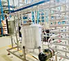 Industrielle Anlage mit Metallrohren, Gestellen und einem großen zylindrischen Behälter in einer Werkhalle.