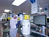 Person in Schutzkleidung bedient Anlagen in einer Produktionshalle mit Edelstahlbehälter und Monitor.