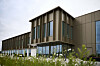 Modernes Bürogebäude mit Glasfront und brauner Verkleidung hinter einer Blumenwiese.