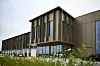 Modernes Bürogebäude mit Glasfront und brauner Verkleidung hinter einer Blumenwiese.