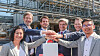 Gruppe von Mitarbeitenden stapelt Hände vor einer Industrieanlage.