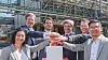 Gruppe von Mitarbeitenden stapelt Hände vor einer Industrieanlage.