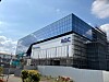 Glasgebäude mit agc-Logo, umgeben von Gerüsten an einer Baustelle.