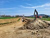 Bagger neben einem Erdwall an einer offenen Baugrube auf einem Feldweg in ländlicher Umgebung.