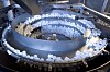 Weiße Kunststoffteile bewegen sich in einer runden Förderanlage in einer Fabrikumgebung.