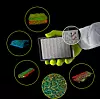 Behandschuhte Hand hält ein Organ-on-a-Chip-Plattform, umgeben von bunten digitalen Visualisierungen auf schwarzem Hintergrund.
