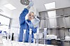 Person im blauen Schutzanzug pipettiert im Labor neben mehreren Glasbehältern.