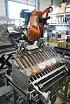 Orangefarbener Industrieroboter in einer Fabrik an einer Verpackungsmaschine mit eingeschweißten Produkten.