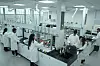 Mehrere Personen in Laborkitteln arbeiten an Geräten in einem hellen Labor.