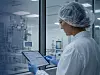 Frau in Schutzkleidung hält ein Tablet in einem Reinraum und kontrolliert Daten.