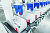 Reihe weiß-blauer Maschinenmodule in einer hellen Fabrikhalle entlang eines Förderbands.