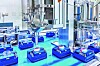 Automatisierte Produktionsanlage mit mehreren kleinen Behältern auf einem Förderband in einer Fabrikhalle.