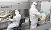 Zwei Personen in Schutzanzügen arbeiten an einer Maschine in einem sterilen Labor.
