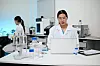 Zwei Wissenschaftlerinnen im Labor mit Laptop, Laborgeräten und Proben auf dem Tisch.