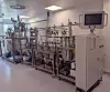 Moderne Industrieanlage aus Edelstahl mit Rohrleitungen und Steuerbildschirm in einem hellen Raum.