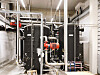 Technischer Raum mit schwarzen Rohrleitungen, Ventilen und Pumpen in einer Industrieanlage.
