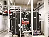 Technischer Raum mit schwarzen Rohrleitungen, Ventilen und Pumpen in einer Industrieanlage.