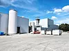 Industrieanlage mit großen Metalltanks, Hallen und befestigtem Hof bei sonnigem Wetter.