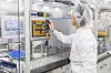 Person in Schutzkleidung bedient ein Steuerpanel in einer automatisierten Produktionsanlage.