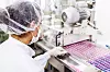 Mitarbeiterin prüft rosa Tabletten auf einer Produktionslinie in einer Arzneimittelfabrik.