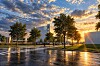 Modernes Bürogebäude bei Sonnenuntergang mit reflektierendem nassem Asphalt und Bäumen im Vordergrund.