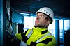 Techniker in Warnweste und Helm prüft elektrische Anlagen in einer Industriehalle.